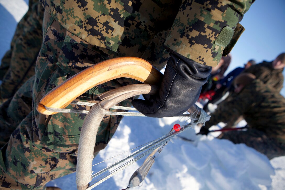 A sailor with 4th Medical Battalion, 4th Marine Logistics Group, Marine Forces Reserve holds an Inupiaq fishing rod as other service members dig a hole in the ice covering Kotzebue Sound, April 17.  Marines and sailors used these authentic Native American ice fishing rods made out of wood to catch 3 fish, April 11, but unsuccessfully did not catch anything on the following fishing trip, April 17. 