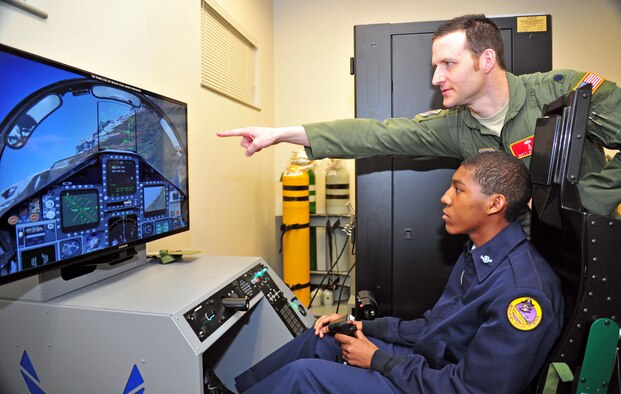 Lt. Col. Matthew Albright, 92nd Aerospace Medicine Squadron aerospace physiological training flight commander, instructs a student of the Junior Reserve Officer Training Corps from Rogers High School on an aircraft piloting simulator at Fairchild Air Force Base, Wash., April 19, 2013. The students received a base tour that held stops at the survival, evasion, resistance and escape water survival training facility, physiology and the military working dog section. (U.S. Air Force photo by Senior Airman Taylor Curry)