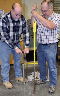 Material engineering technician Joe Kissel (right) compares their homemade time-of-set device to the standard device displayed by Lance Lawyer, a quality control technician with the joint venture WGA. (U.S. Army Corps of Engineers photo by Jon Fleshman)