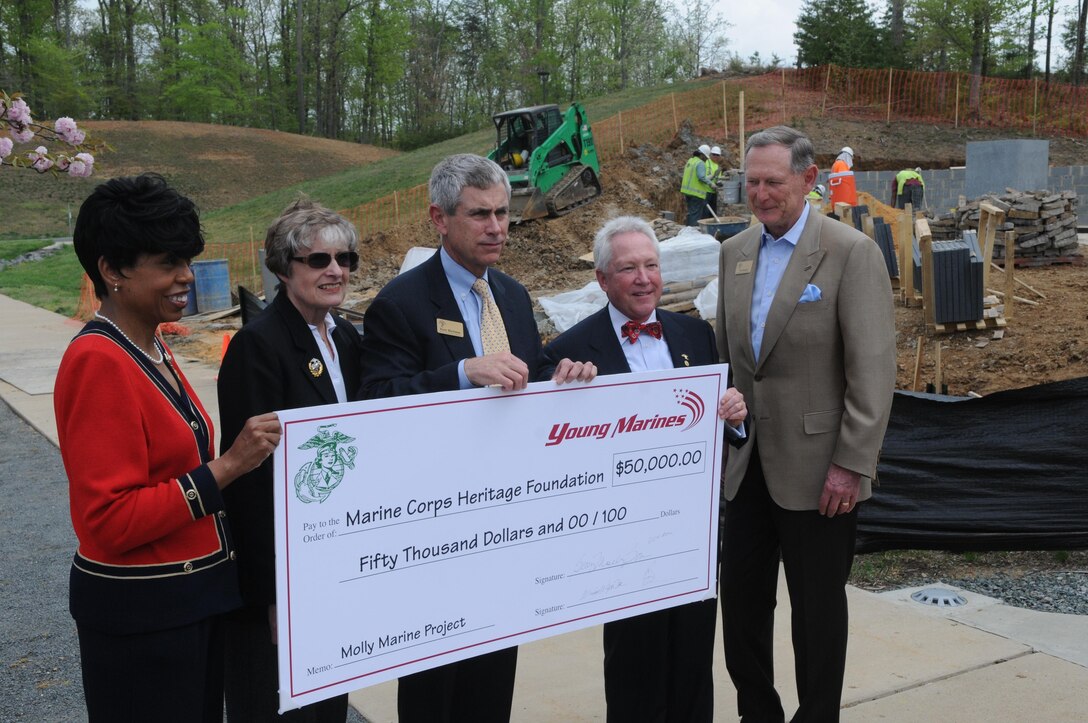 From left, Betty Moseley-Brown, president of the Women Marines Association; retired Lt. Gen. Carol Mutter, former WMA president; retired Lt. Gen. Rusty Blackman, president of the Marine Corps Heritage Foundation; Gerry Reis, chairman of the board of the Young Marines; and retired Gen. Walt Boomer, chairman of the board of the MCHF, pose with a novelty check representing the Young Marines’ $50,000 donation to the Molly Marine project under construction behind them at the National Museum of the Marine Corps. 