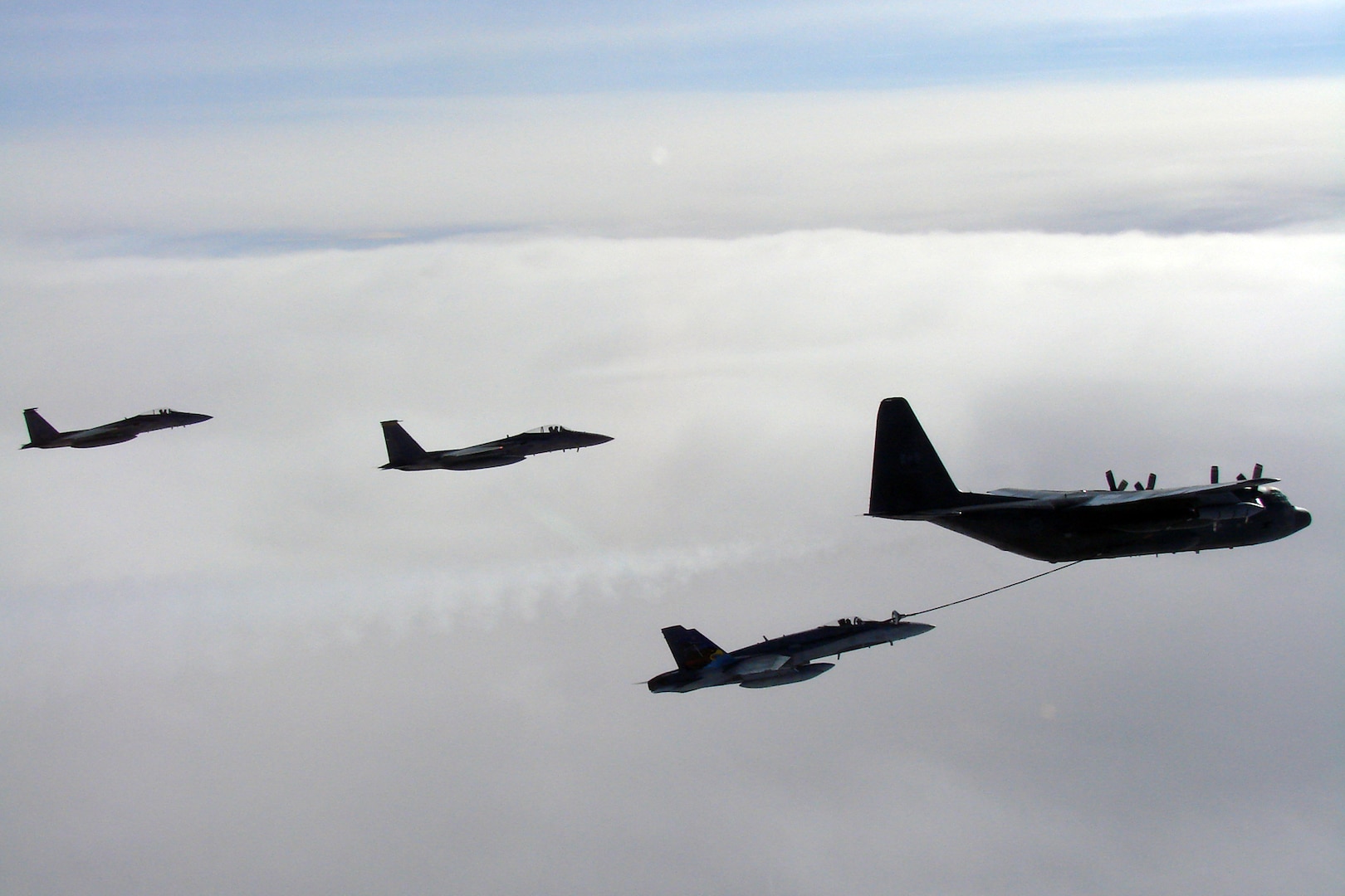 A CF-18 Hornet tops up its tanks from a CC-130T Hercules, both from the Canadian North American Aerospace Defense Command Region, while two F-15 Eagles from Elmendorf Air Force Base, Alaska, fly nearby. The aircraft were in the Canadian north in March 2007 to practice joint long-range detection missions and other NORAD procedures.
