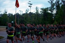 Marines and sailors with 2nd Marine Logistics Group run towards Soifert field during a unit three-mile run aboard Camp Lejeune, N.C., April 25, 2013. A Marine holds his company flag high in the sky showing his unit pride as the platoon yells cadences.
