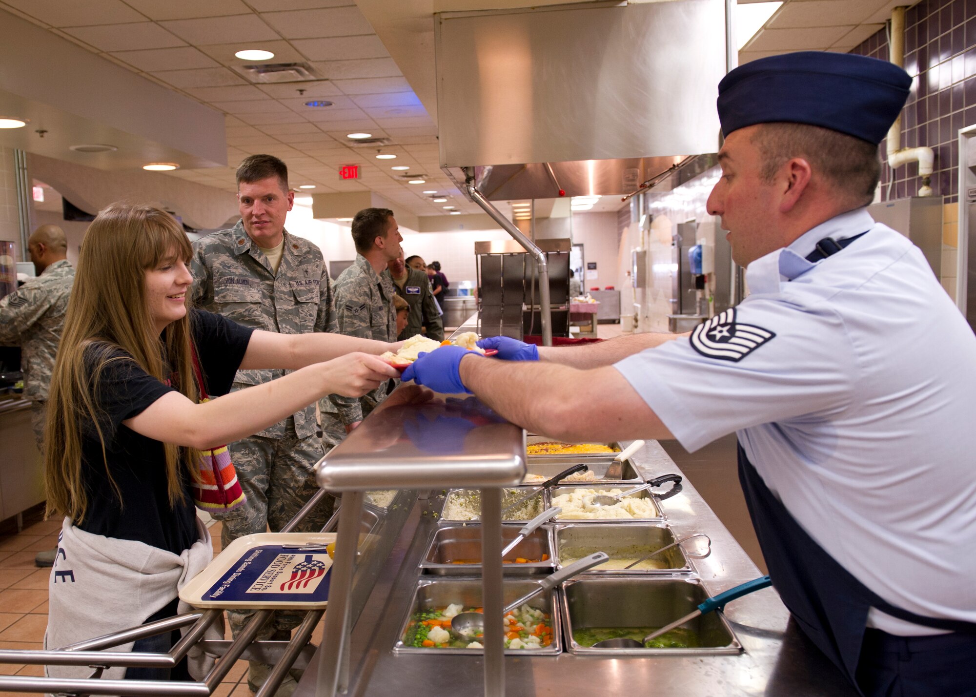 Tech. Sgt. William Lodin, 49th Force Support Squadron Shifting Sands Dining Facility assistant manager, gives Emely Von Almen her plate while having lunch with her father, Maj. John Von Almen, 49th Wing deputy chaplain, during Take Your Kid to Work Day at Holloman Air Force Base, N.M., April 22. Emely spent the day with her father learning what he does on a daily basis. (U.S. Air Force photo by Senior Airman Kasey Close/Released)