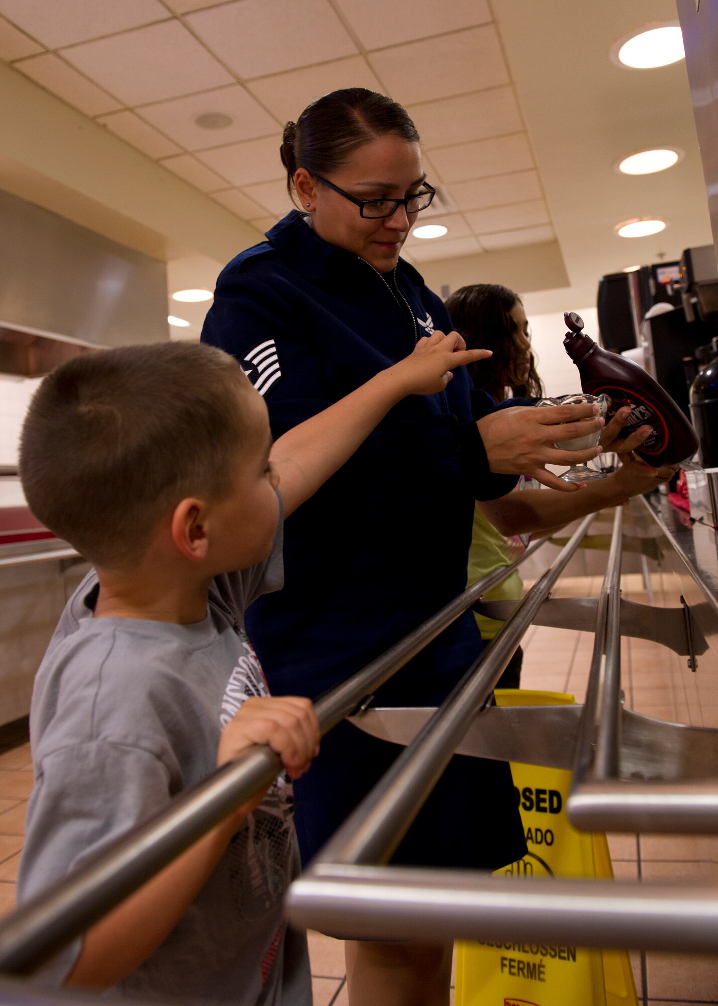 Tech. Sgt. Erica Jordan, 49th Wing command chief assistant, finishes pouring chocolate sauce over her son’s ice cream while having lunch at the Shifting Sands Dining Facility during Take Your Kid to Work Day at Holloman Air Force Base, N.M., April 22. The event was held in April for the Month of the Military Child. (U.S. Air Force photo by Senior Airman Kasey Close/Released)