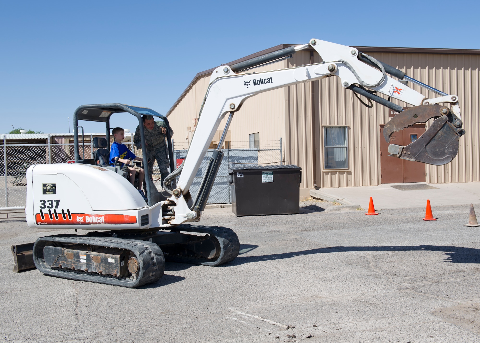Senior Airman Leonel Lopez, 49th Civil Engineer Squadron heavy equipment operator, shows Keelin Cueavas how to operate a mini excavator during Take Your Kid to Work Day at Holloman Air Force Base, N.M., April 22. Keelin is the son of Master Sgt. Michael Cueavas, 49th CES first sergeant. (U.S. Air Force photo by Senior Airman Kasey Close/Released)