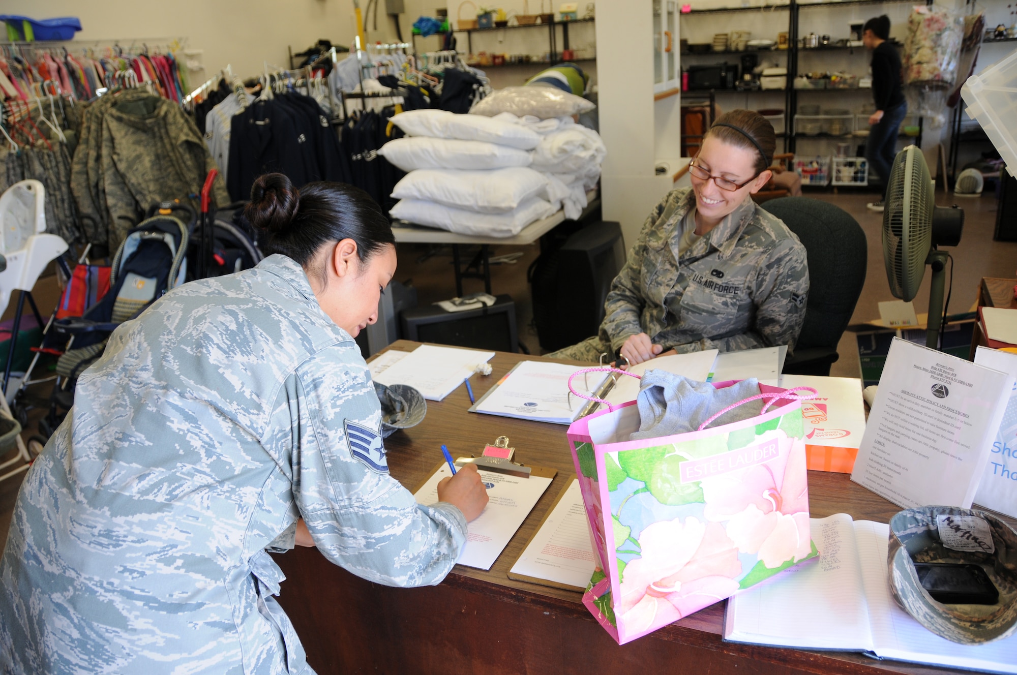 Staff Sgt. Connie Martinez (left), Air Force Mortuary Affairs Operations, lists a description of the items she chose from the display racks at the Airman's Attic, April 24, 2013, Dover Air Force Base, Del. Airman 1st Class Lori Cord, 436th Aircraft Maintenance Squadron, is one of  the organization's volunteers who spends her free time assisting Attic patrons with their selections. (U.S. Air Force photo/Senior Airman Joe Yanik) 