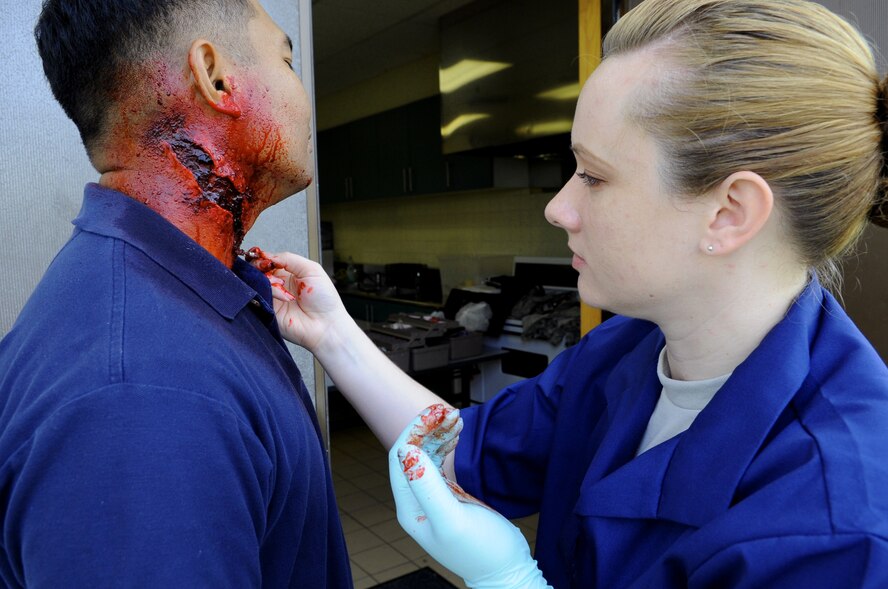 U.S. Air Force Staff Sgt. Marie Thomas, 18th Dental Squadron dental lab craftsman, applies stage make-up upon the neck of Staff Sgt.  Ronann Andres, 18th Civil Engineer Squadron water and fuels system maintenance craftsman, on Kadena Air Base, Japan, April 24, 2013. Thomas used the make-up to help simulate a neck injury to Andres that would leave him dead during a simulated tour bus crash during the emergency management exercise. (U.S. Air Force photo by Airman 1st Class Keith A. James/Released)