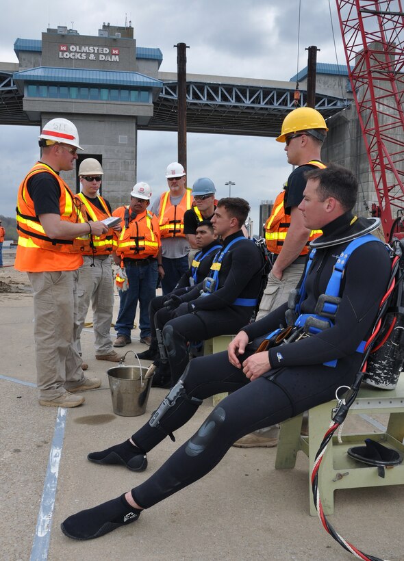 Staff Sgt. Kyle Broughton (left) goes through the pre-dive safety check and final instructions with the primary divers, backup and support staff on the Olmsted middle lock wall. The wet-suited divers on the benches that day are: (left to right) Sgt. (P) Patrick Morales, Spc. Jacob "The Fireball" Feyers and Spc. Thomas Dougherty.