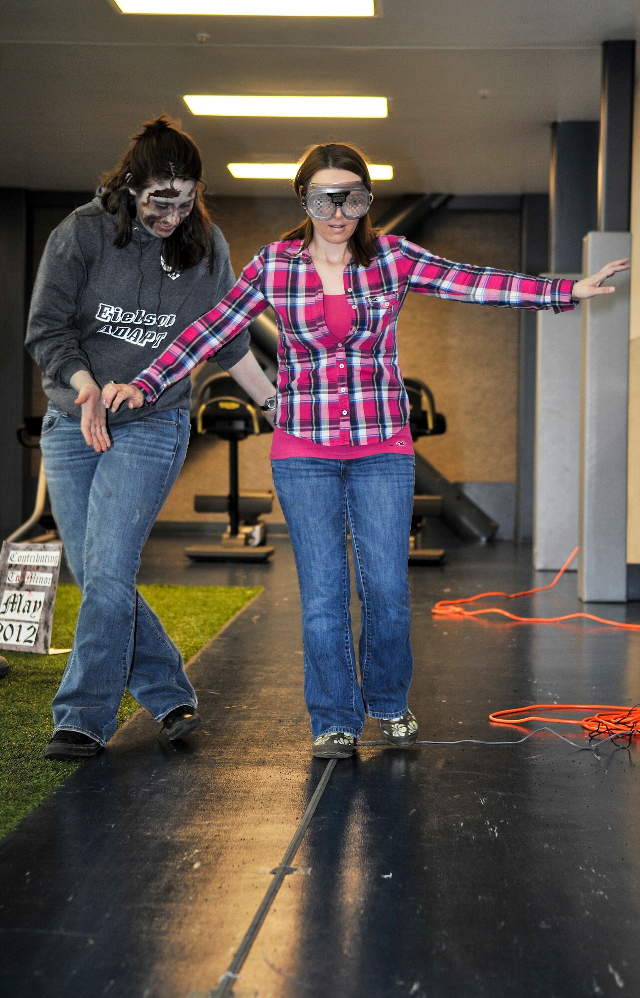 U.S. Air Force Staff Sgt. Mallory Lass, 354th Medical Group Alcohol and Drug Abuse Prevention and Treatment volunteer, assists Christy Hedrick, wife of Master Sgt. Ricky Hedrick, 354th Maintenance Squadron conventional maintenance NCO in charge, walk a straight line while wearing beer goggles during an alcohol awareness event at the fitness center April 18, 2013, Eielson Air Force Base, Alaska. Eielson’s ADAPT team offered hands-on experiences demonstrating how the body reacts while inebriated. (U.S. Air Force photo by Senior Airman Racheal E. Watson/Released)