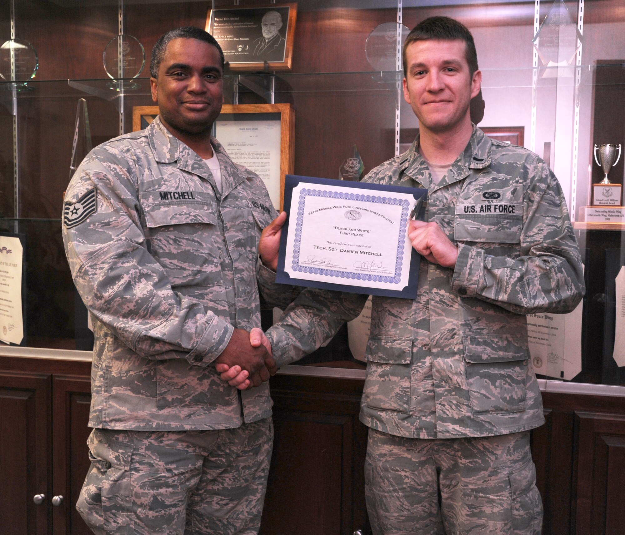 Tech. Sgt. Damien Mitchell, 819th RED HORSE Squadron airfields NCO in charge, left, receives a certificate and coin from 1st Lt. Chase McFarland, 341st Missile Wing Public Affairs assistant chief, for his first place entry in the 341st MW Public Affairs Quarterly Amateur Photo Contest on April 19. Mitchell’s photo of a street musician in Omaha, Neb., expertly encompassed last quarter’s theme, “Black and White.” (U.S. Air Force photo/Airman 1st Class Katina Heikkinen)