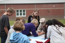 A Marine with Combat Logistics Regiment 27, 2nd Marine Logistics Group teaches students how to plot points on a map using a protractor at Brewster Middle School during a land navigation class aboard Camp Lejeune, N.C., April, 25 2013. The students applied what they learned to locate empty ammunition containers hidden in the field behind the school.
