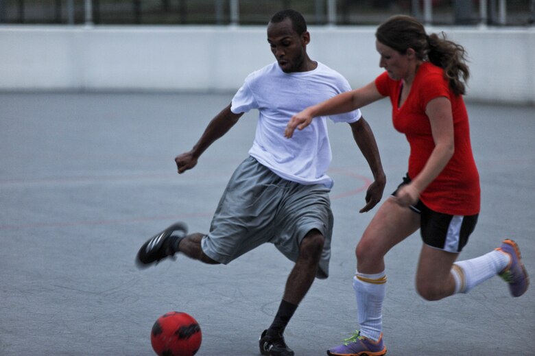 Senior Airman Ian Brooks, soccer player for the Special Tactics Training Squadron Team, attempts a shot at the goal as Shana Cumberworth, soccer player for Team Red, attempts to intercept during an arena soccer game at the Riptide Fitness Center’s hockey arena on Hurlburt Field, Fla, April 12, 2013. (U.S. Air Force photo by Senior Airman Kentavist P. Brackin)