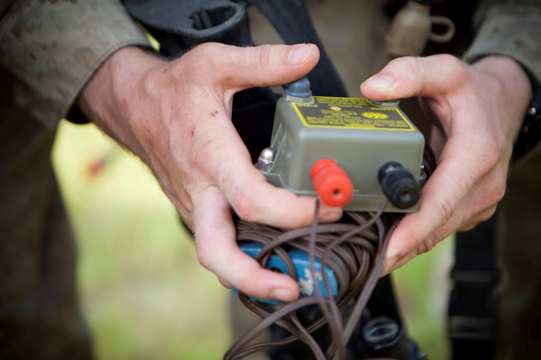 A Sapper Leadership Course student charges a CD 450-J ignition device during rehearsal for the urban demolition range, July 24, 2013. The device, also called a “j-box,” is a lightweight, battery-operated blasting device that the combat engineers used during urban demolition. The device requires a Marine to hold a “charge” button and count-off loudly until the “ready to fire” indicator lights up. At that moment, the breacher will push the “fire” button, igniting the explosion. 