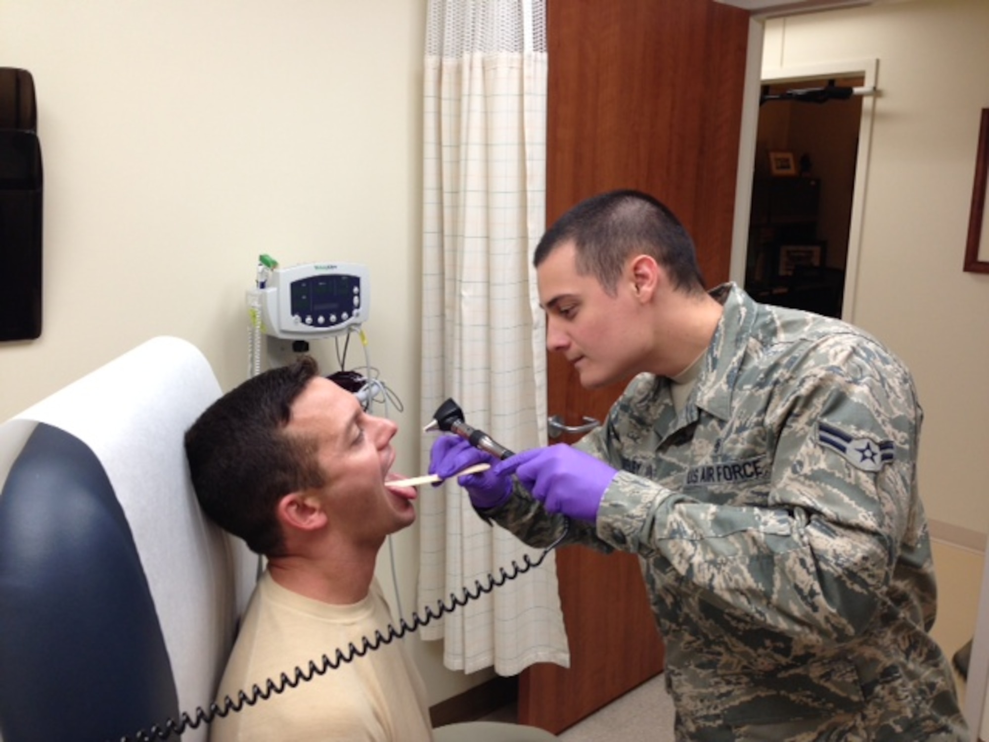Airman 1st Class Casey Blakely, 341st Medical Operations Squadron technician, right, performs a throat examination on Staff Sgt. Michael Canfield, 341st MDOS technician, at the Family Health Clinic and Pediatric department on July 25. The base clinic now offers walk-in sore throat examinations and test results notification. (Courtesy photo)