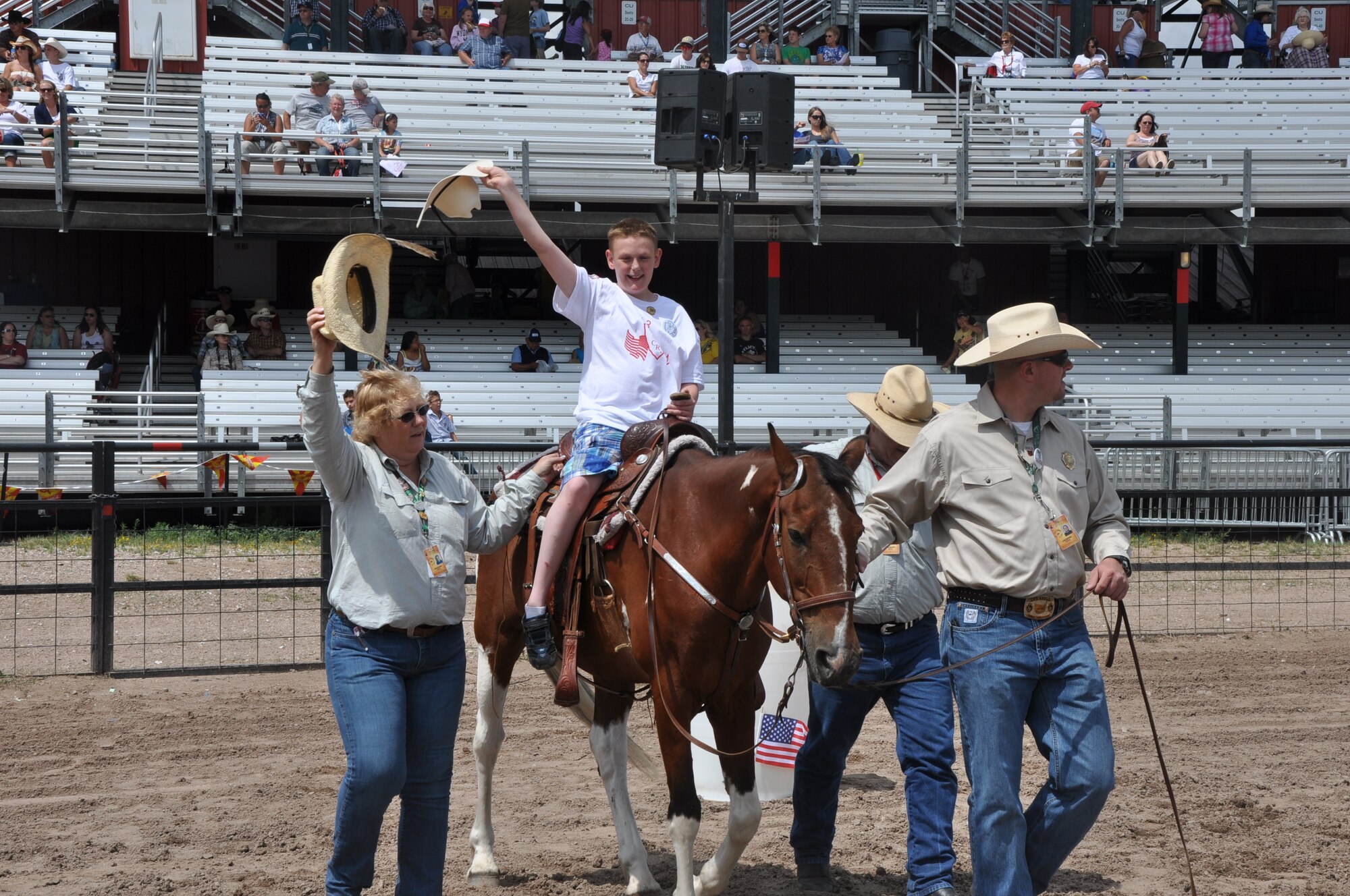A child holds his hat high as he waves to the crowd July 24, 2013, during the Cheyenne Frontier Days Challenge Rodeo event held in Frontier Park, Cheyenne, Wyo., as volunteers help steady the horse. (U.S. Air Force photo by Airman 1st Class Brandon Valle)