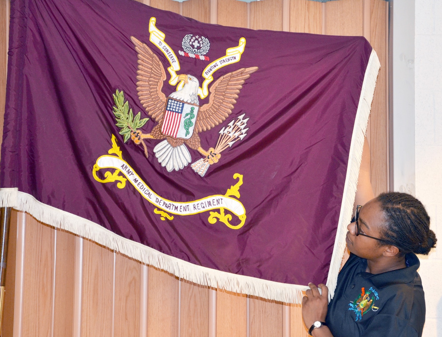 Sgt. Audie Murphy Club member Sgt. 1st Class Tiffany Skelton holds up the Army Medical Department Regimental Flag as the keynote speaker at the 27th anniversary celebration describes what each symbol represents. (Photo by Esther Garcia, U.S. Army Medical Department Center and School Public Affairs) 