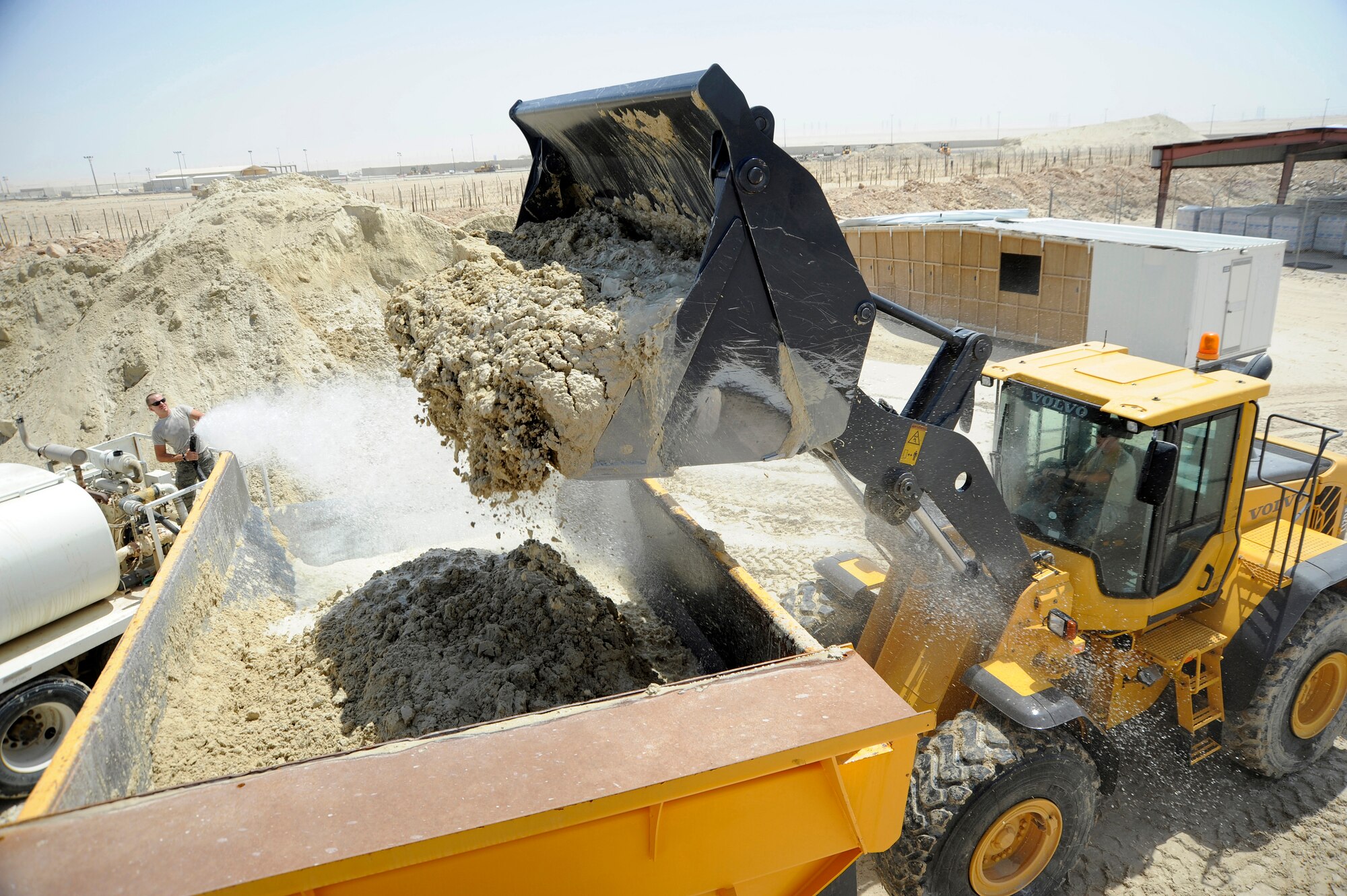 Tech. Sgt. Justin Kearns, 386th Expeditionary Civil Engineer Squadron, uses a water truck to douse the gatch while Senior Airman Nicholas Moxley, 386th ECES, loads it into a 30-ton dump truck with a Volvo loader here, July 24, 2013. Kearns and Moxley are both heavy equipment operators. Kearns is watering down the gatch to put moisture into it making it easier to bond. Gatch is a sand and gypsum mix used under all buildings here; it is the equivalent to quick concrete. Kearns, a native of Reed City Mich. is deployed out of the 110th Airlift Wing, Battle Creek, Mich., Air National Guard unit. Moxley, a native of Shippensburg, Pa. is deployed out of Holloman Air Force Base, N. M. (U.S. Air Force photo by Master Sgt. Christopher A. Campbell)