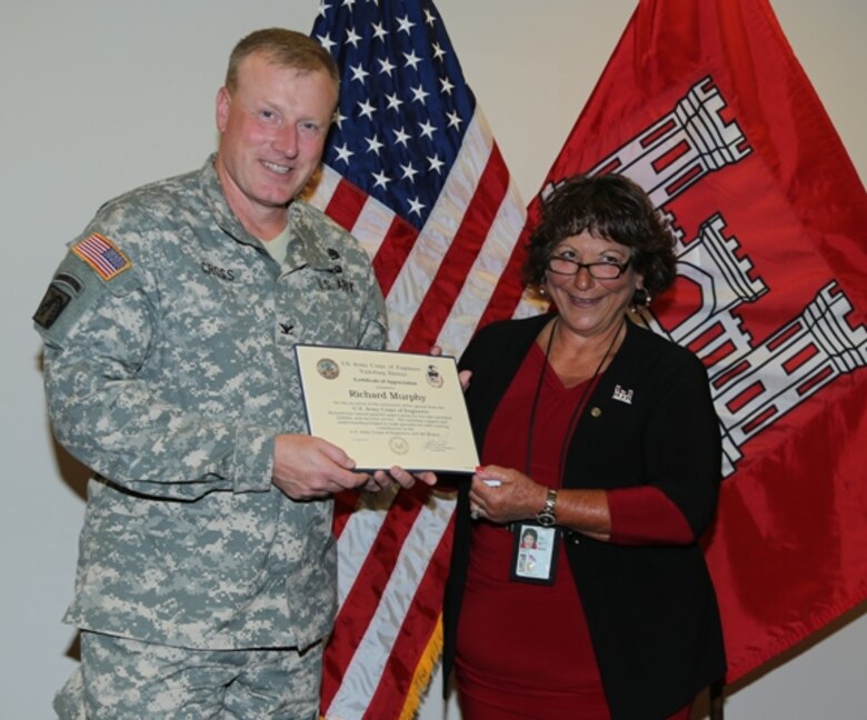 Vicksburg, Miss… Carol Ann Murphy of the U.S. Army Corps of Engineers Vicksburg District is retiring after 26 years of service.  

Murphy began her career in the Contracting Office as a procurement technician and later transferred to the Safety Office as an office administration assistant. Mrs. Murphy accepts an award for her husband Richard Murphy from Col John Cross, the Vicksburg District Commander.