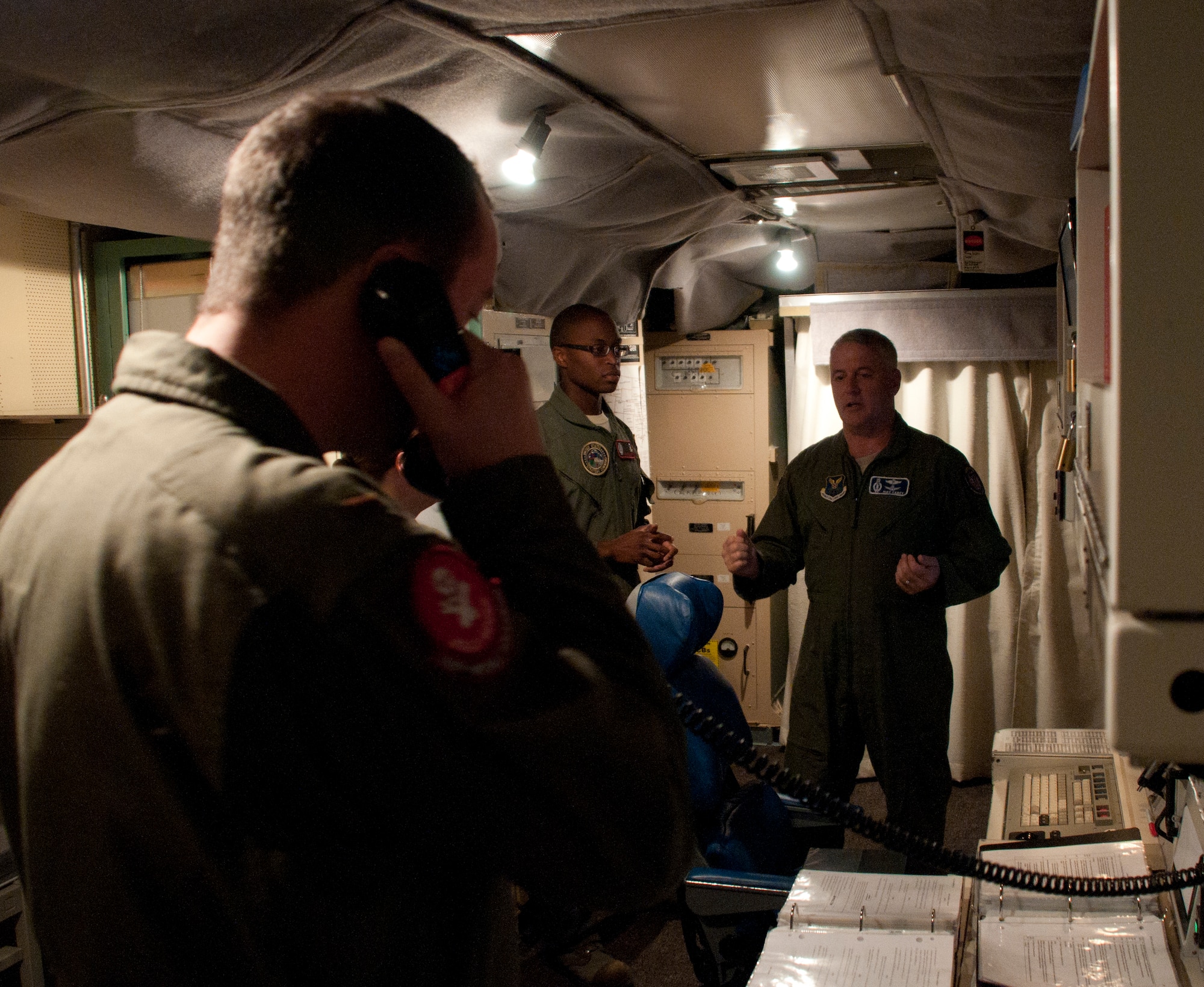 Second Lt. Nicholas Tramutolo, 320th Missile Squadron deputy missile combat crew commander, answers a phone to discuss duty-related matters while Capt. Keidrick Roy, 320th MS missile combat crew commander, speaks with Maj. Gen. Michael Carey, 20th Air Force commander, in the launch control center of the Foxtrot-01 Missile Alert Facility July 29, 2013. (U.S. Air Force photo by Airman 1st Class Jason Wiese)