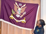 Sgt. Audie Murphy Club member Sgt. 1st Class Tiffany Skelton holds up the Army Medical Department Regimental Flag as the keynote speaker at the 27th anniversary celebration describes what each symbol represents. (Photo by Esther Garcia, U.S. Army Medical Department Center and School Public Affairs) 