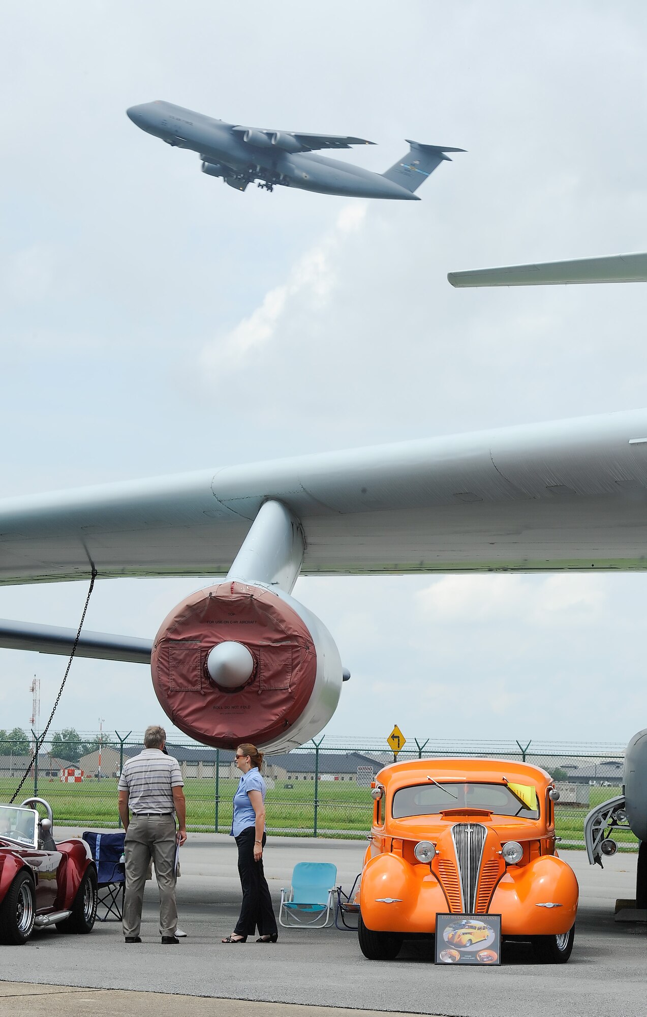 Classic cars sit under the wing of a C-141A Starlifter at the Air Mobility Command museum while a C-5M Super Galaxy flys in the background. Dozens of cars joined the museum's aircraft on display for the 2013 Wings and Wheels car show on July 28, 2013. Courtesy photo by Greg L. Davis