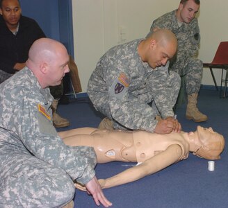 Pennsylvania Army National Guardsman Sgt. 1st Class Ronald James (left), the noncommissioned officer in charge of the mobile training team teaching combat life saver skills to 21st Theater Sustainment Command Soldiers at Panzer Kaserne, keeps a close eye on a Soldier, who is practicing his needle-chest decompression skills March 25.