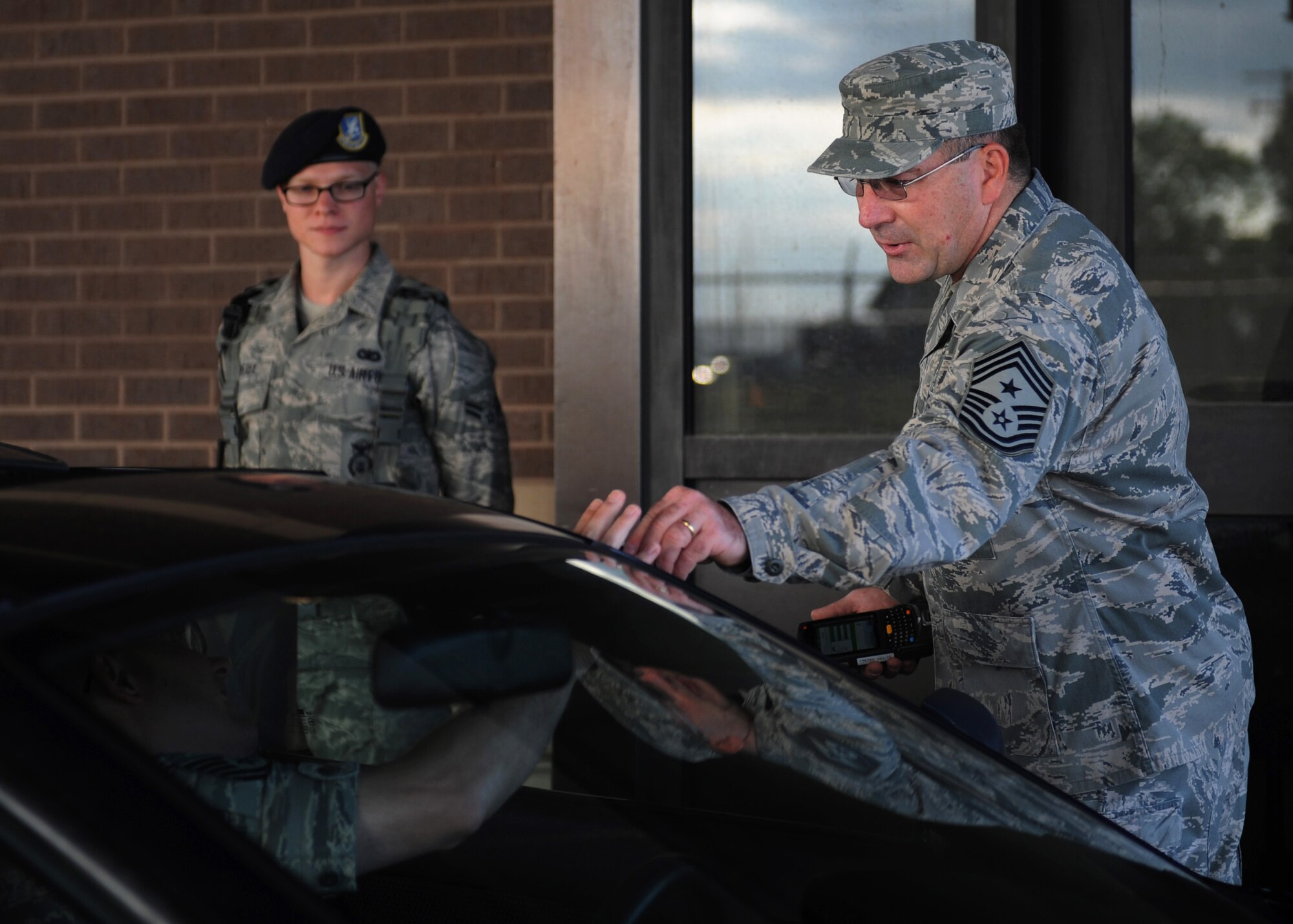 Chief Master Sergeant Kevin Peterson, 28th Bomb Wing command chief, checks identification cards at the Patriot Gate with Airman 1st Class Travis Overly, 28th Security Forces Squadron defender, at Ellsworth Air Force Base, S.D., July 30, 2013. The chief will be visiting various work sections across the base meeting with Airmen to better understand their daily tasks and to experience firsthand challenges they face each day. (U.S. Air Force photo by Airman 1st Class Rebecca Imwalle/Released)