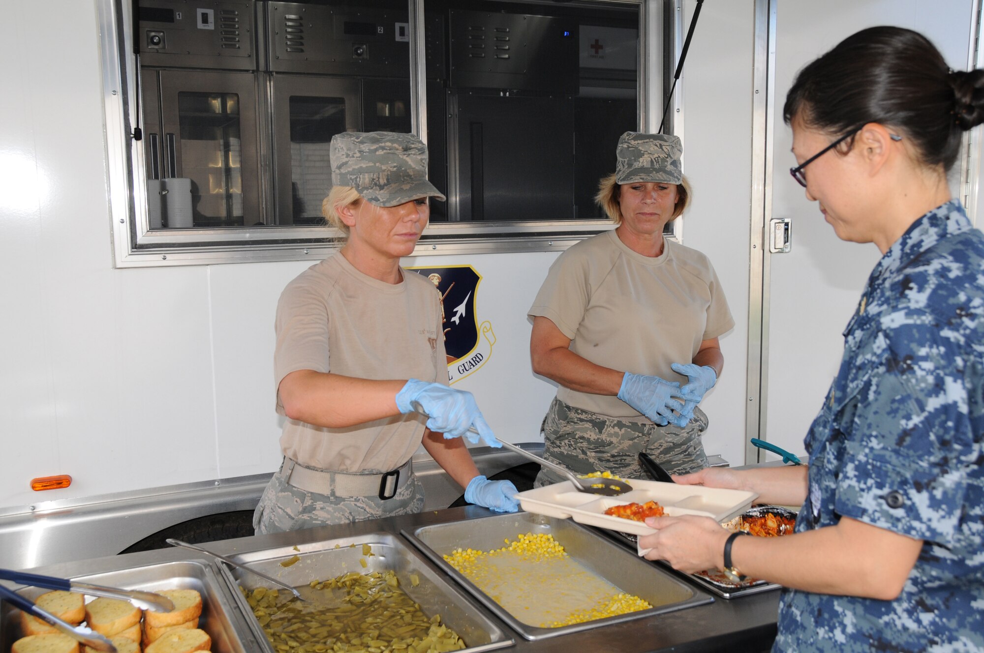 U.S. Air Force Tech. Sgt. Donna Hooper (left) and Master Sgt. Krista Lindsey, Force Support Flight, 123d Airlift Wing, Louisville, Kentucky, serve lasagna in front of a Disaster Response Mobile Kitchen Trailer (DRMKT) July 15 at ‘Hope of Martin’ Innovative Readiness Training held at Martin Middle School in Martin, Tenn. (U.S. Air National Guard photo by Master Sgt. Carlos J. Claudio/Released).