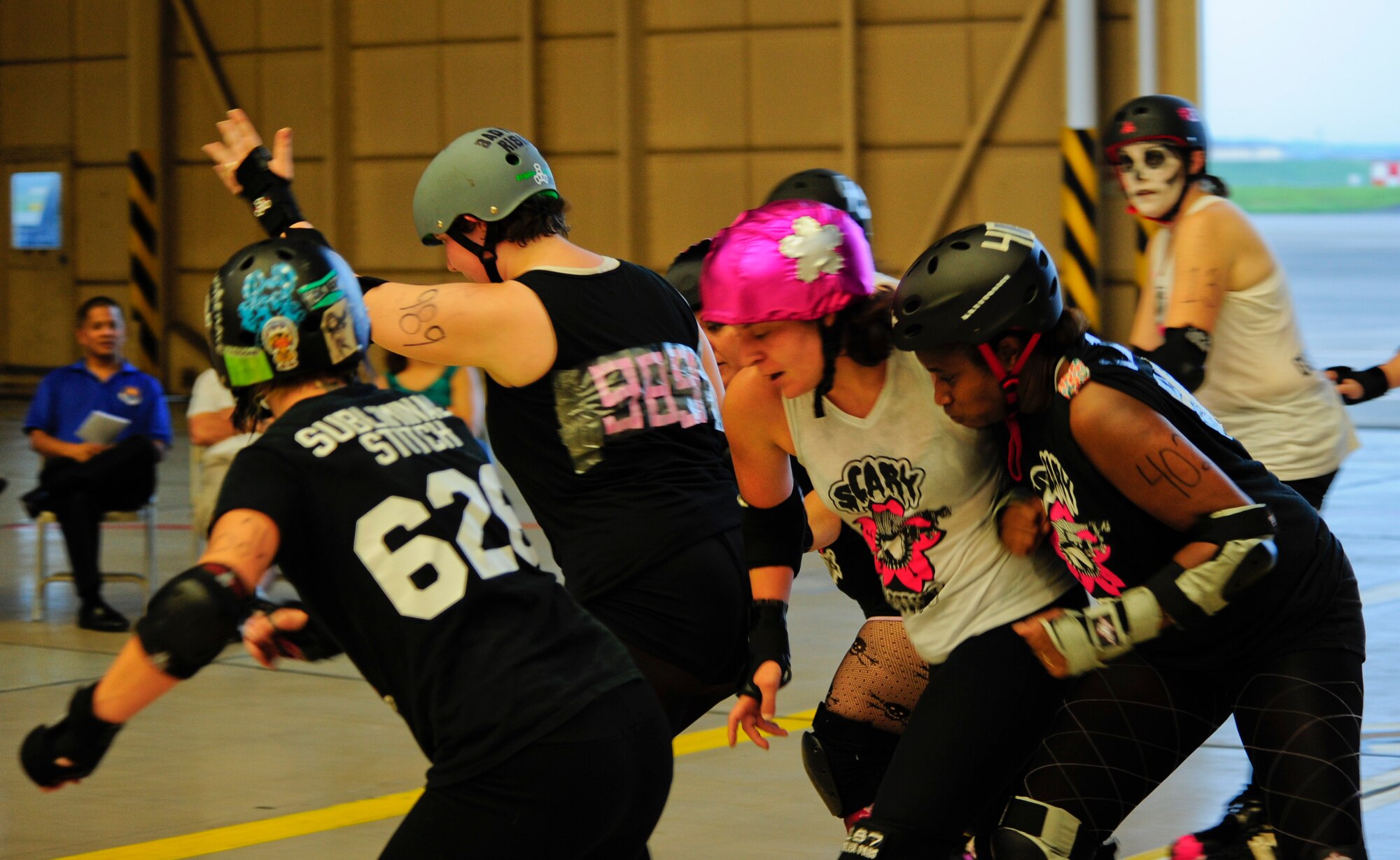 A jammer on the Skeleton team (white shirt) battles her way past members of the Reapers during the Scary Blossoms’ inner-team bout inside Hangar 15 at Yokota Air Base, Japan, July 27, 2013. Derby team positions consist of a jammer, who scores the points for the team; blockers, who try to stop the jammer; and the pivot, who regulates the pack speed and may become jammers during the duration of the jam – a two minute period in which the action happens. (U.S. Air Force photo by Senior Airman Michael Washburn)