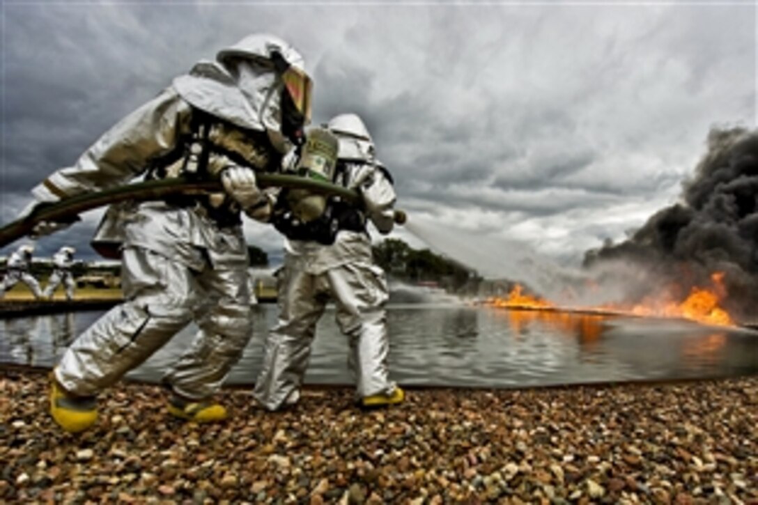 Firefighters maneuver a hose to attack fires to support Warrior and Global Medic exercises on Fort McCoy, Wis., July 27, 2013. Warrior Exercise 86-13-01 enables units to rehearse military maneuvers and tactics. Global Medic 2013 is an annual field training exercise designed to replicate all aspects of theater combat medical support.