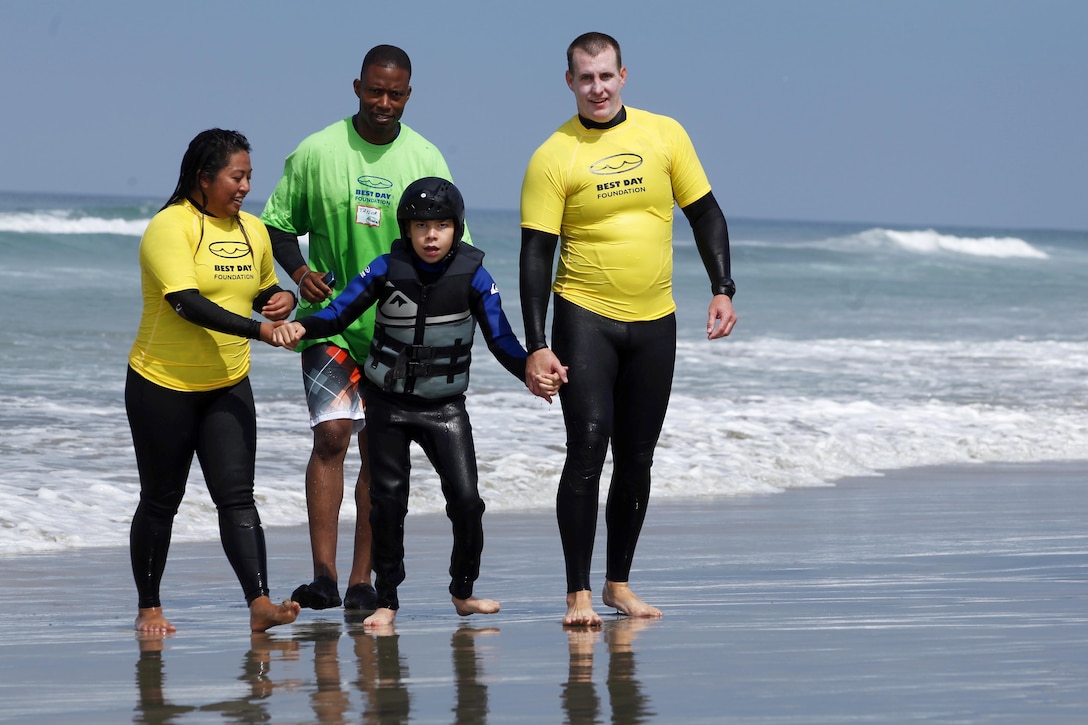 Hunter, 13, is escorted down the beach after riding a surf board back to shore during the award ceremony of  the Exceptional Family Member Program Best Day Beach Event  at Del Mar Beach here Aug. 3. Exceptional Family Member Program participants and volunteers with the Orange County Best Day Foundation spent the day surfing, body boarding and Kayaking in an effort to build self-esteem and confidence in children. 