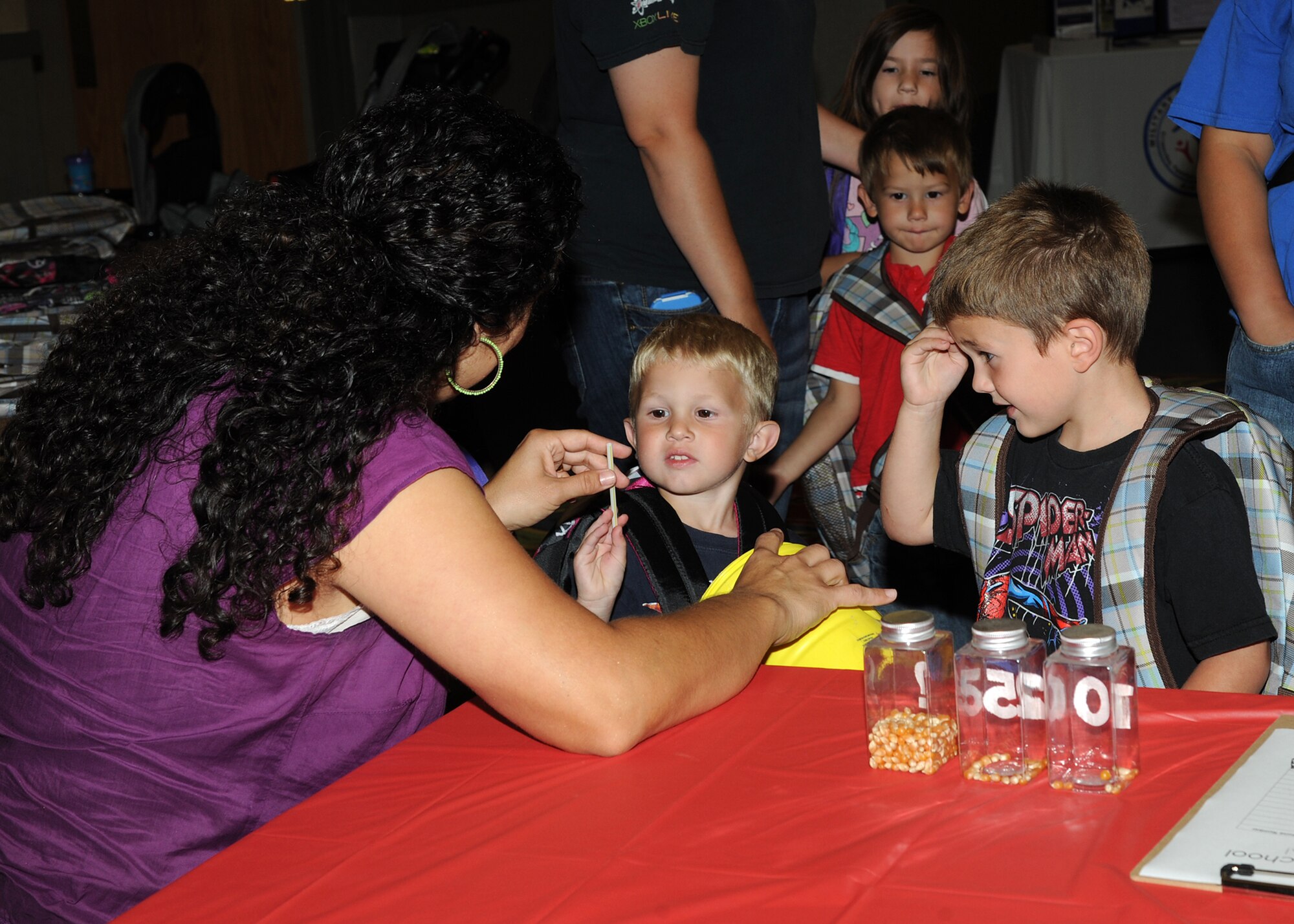 Katie Musgrove, founder and teacher at Pinwheel Preschool, plays a guessing game with brothers Jayce Butters, 3, and Zach Butters, 5, at the Preschool Fair, Aug. 1, 2013, on Grand Forks Air Force Base, N.D. In the guessing game, kids are encouraged to tap into their five senses to guess what an object is based on the sound it makes or how it feels. (U.S. Air Force photo/Senior Airman Ashley Nicole Taylor)