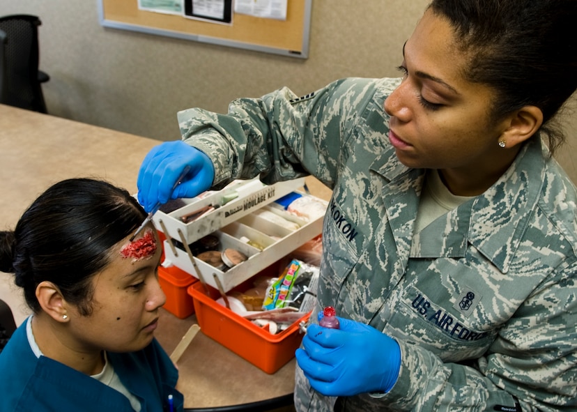 U.S. Air Force Master Sgt. Celeste Okokon, 7th Aerospace Medicine Squadron flight chief, applies make-up to an Airman July 16, 2013, at Dyess Air Force Base, Texas. As the Moulage team chief at Dyess, Okokon creates simulated injuries using realistic make-up to aid in training for crisis events. (U.S. Air Force photo by Airman 1st Class Peter Thompson/Released)