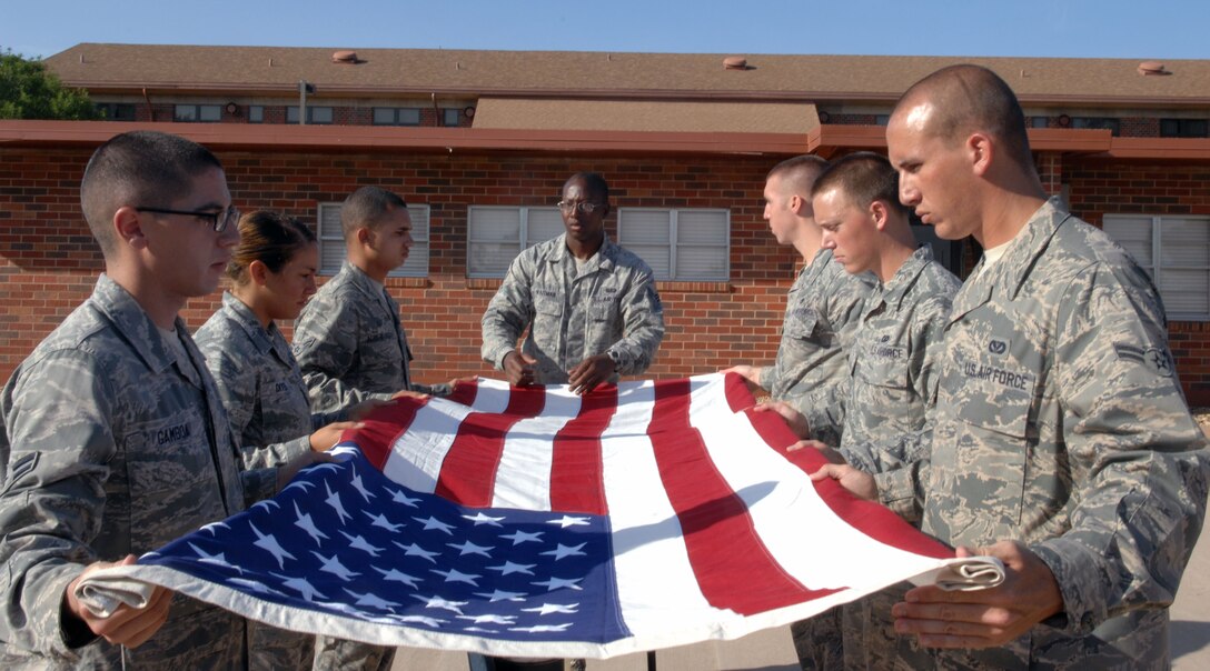 Airmen assigned to the 7th Bomb Wing Honor Guard, hold the American flag at table top position during training week, Aug. 2, 2013, at the honor guard building on Dyess Air Force Base, Texas. Airmen spend three months with the honor guard, traveling around Texas to perform ceremonial duties for deceased service members. Dyess covers 34,000 square miles, 38 counties and perform more than 200 funerals a month. During the funerals the members pallbearer the casket, perform a flag fold, a three-man gun salute, play taps and present the flag and three shell casings to the next-of-kin. (U.S. Air Force photo by Senior Airman Shannon Hall/Released)