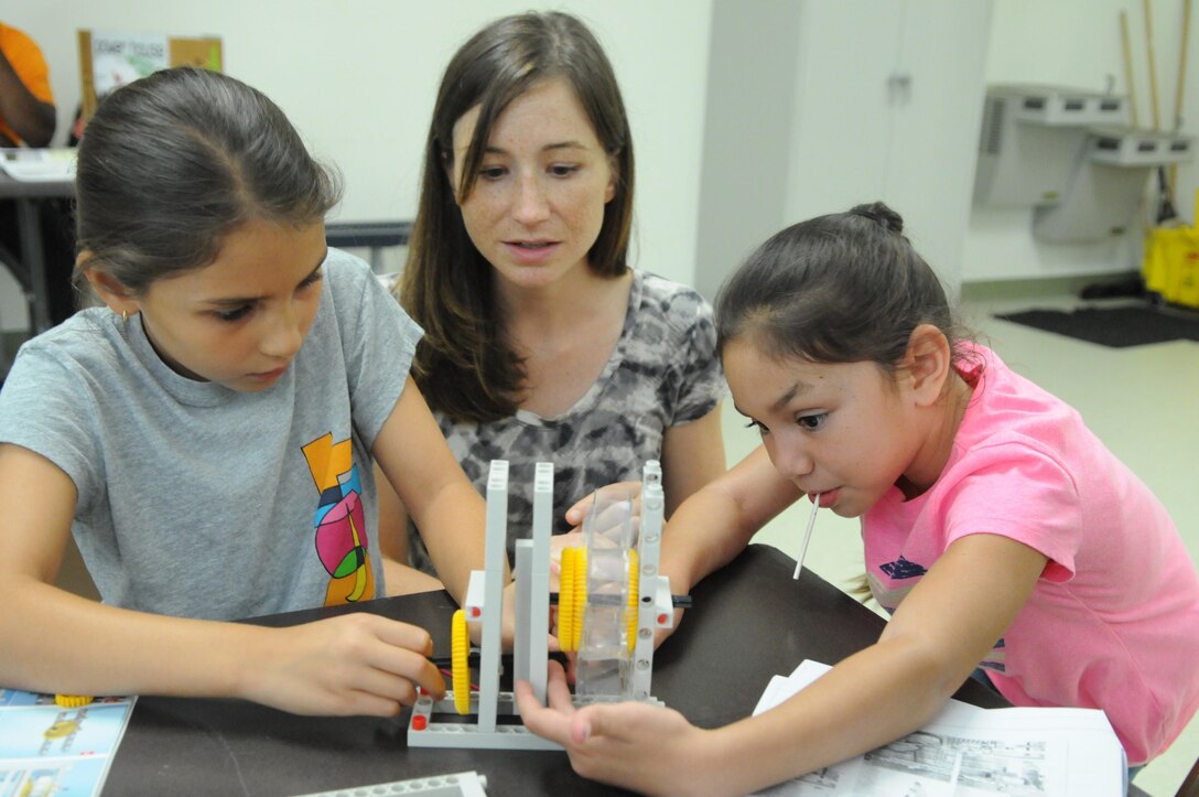 Stefanie Kivelin, base energy manager, oversees while Isabella, 9, left, and Arianna, 8, work on a water wheel-powered generator at the Quantico Youth Center on July 29, 2013. 