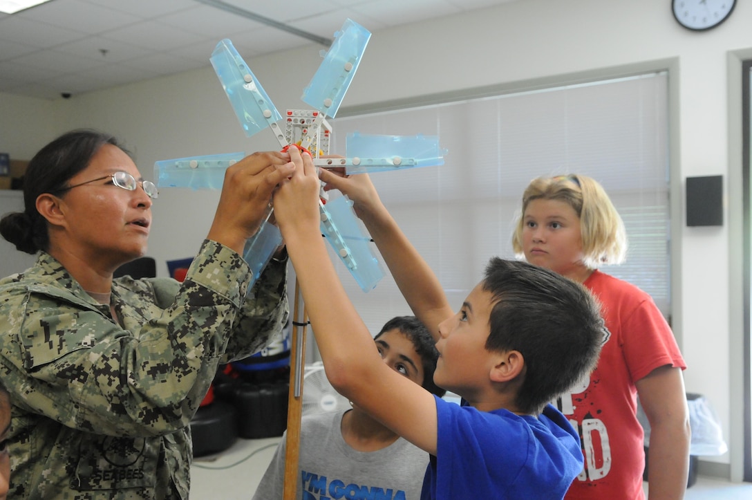 Senior Chief Petty Officer Diane Paddock, Seabee with Quantico Public Works Branch, and Nicholas, 10, attach a windmill to a generator as David and Olivia, both 10, look on at the Quantico Youth Center on July 29. 