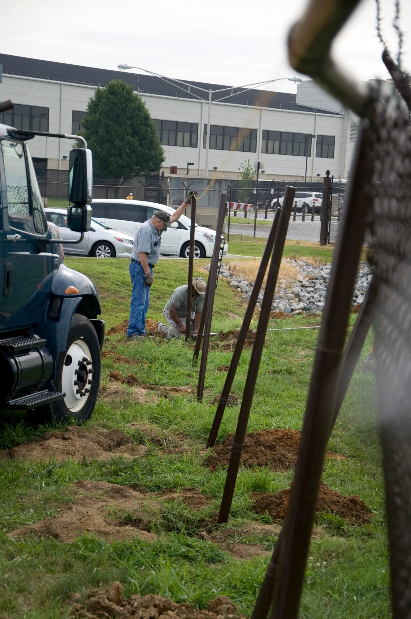 Clyde Wheeler and Jeff Smith, 436th Civil Engineer Squadron pavement and equipment operators, ensure fence posts are in line before positioning concrete July 24, 2013, at Dover Air Force Base, Del. An automobile collided with the base perimeter fence earlier in July causing damage to 200 feet of fencing, costing an estimated $6000. (U.S. Air Force photo/Senior Airman Jared Duhon)