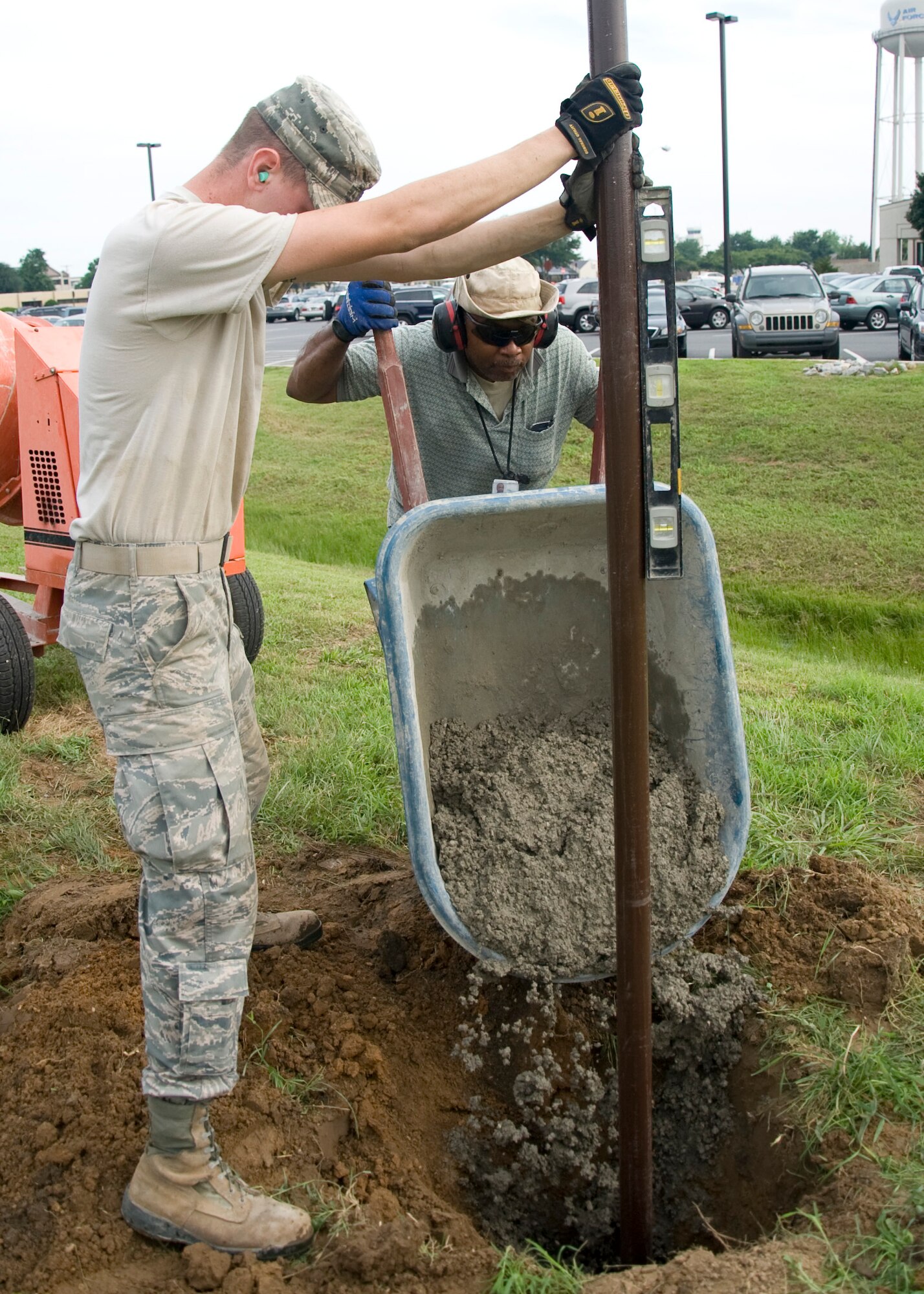 Airman 1st Class Trever Bitterman and  Jeff Smith, 436th Civil Engineer Squadron pavement and equipment operators, pour concrete around a new fence post July 24, 2013, at Dover Air Force Base, Del. The cost of the fence repair was an estimated $6000. (U.S. Air Force photo/Senior Airman Jared Duhon)