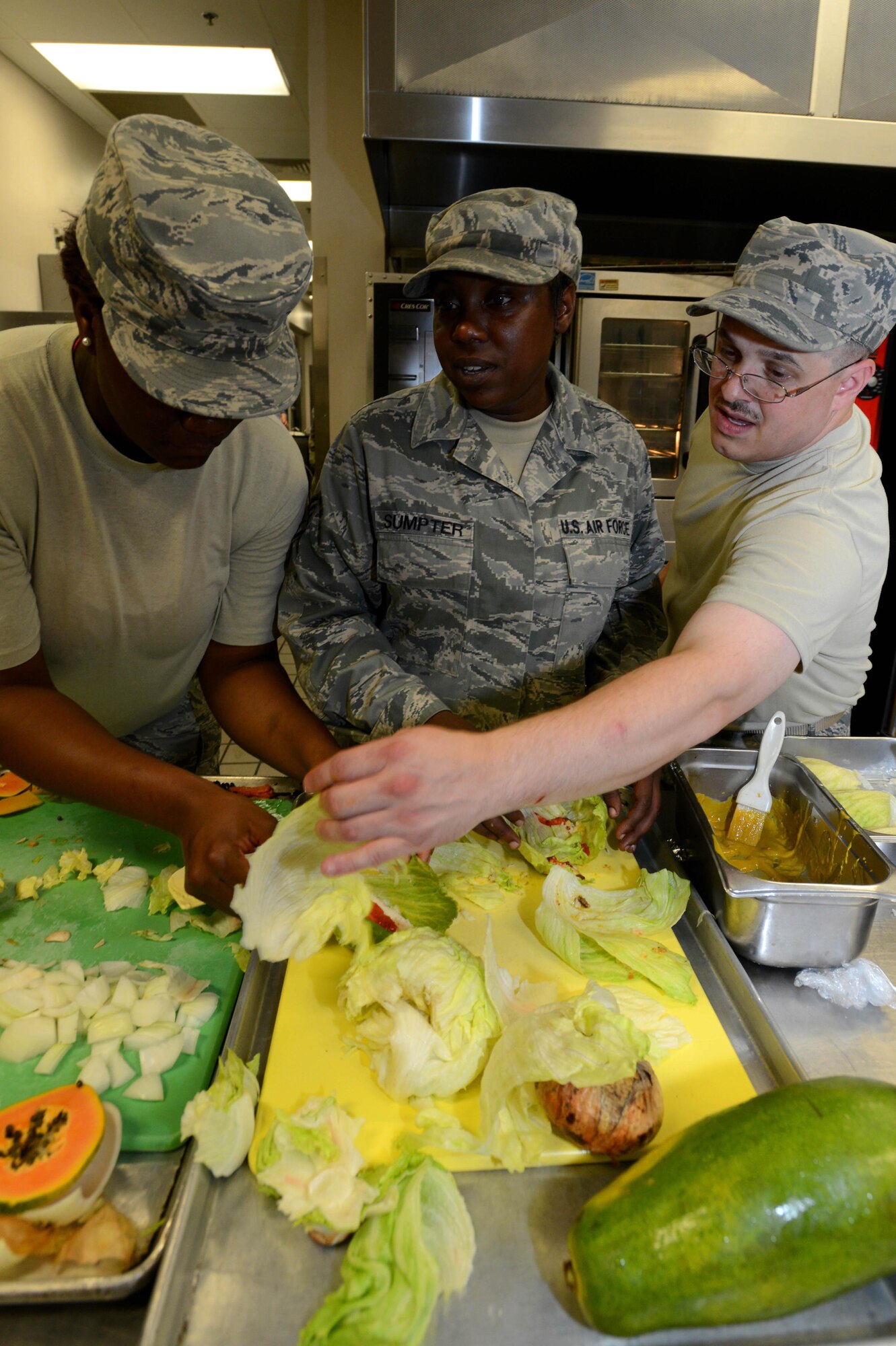 (From left) Staff Sergeants Sethena Butler, Adrienne Sumpter, and Matthew Franklin, 20th Force Support Squadron shift supervisors, rush to finish cooking during an Iron Chef competition at the Chief Master Sgt. Emerson Williams Dining Facility, Shaw Air Force Base, S.C., July 30, 2013. The competition was judged on two dishes prepared with the secret ingredient of papaya. (U.S. Air Force photo by Airman 1st Class Jensen Stidham/Released) 