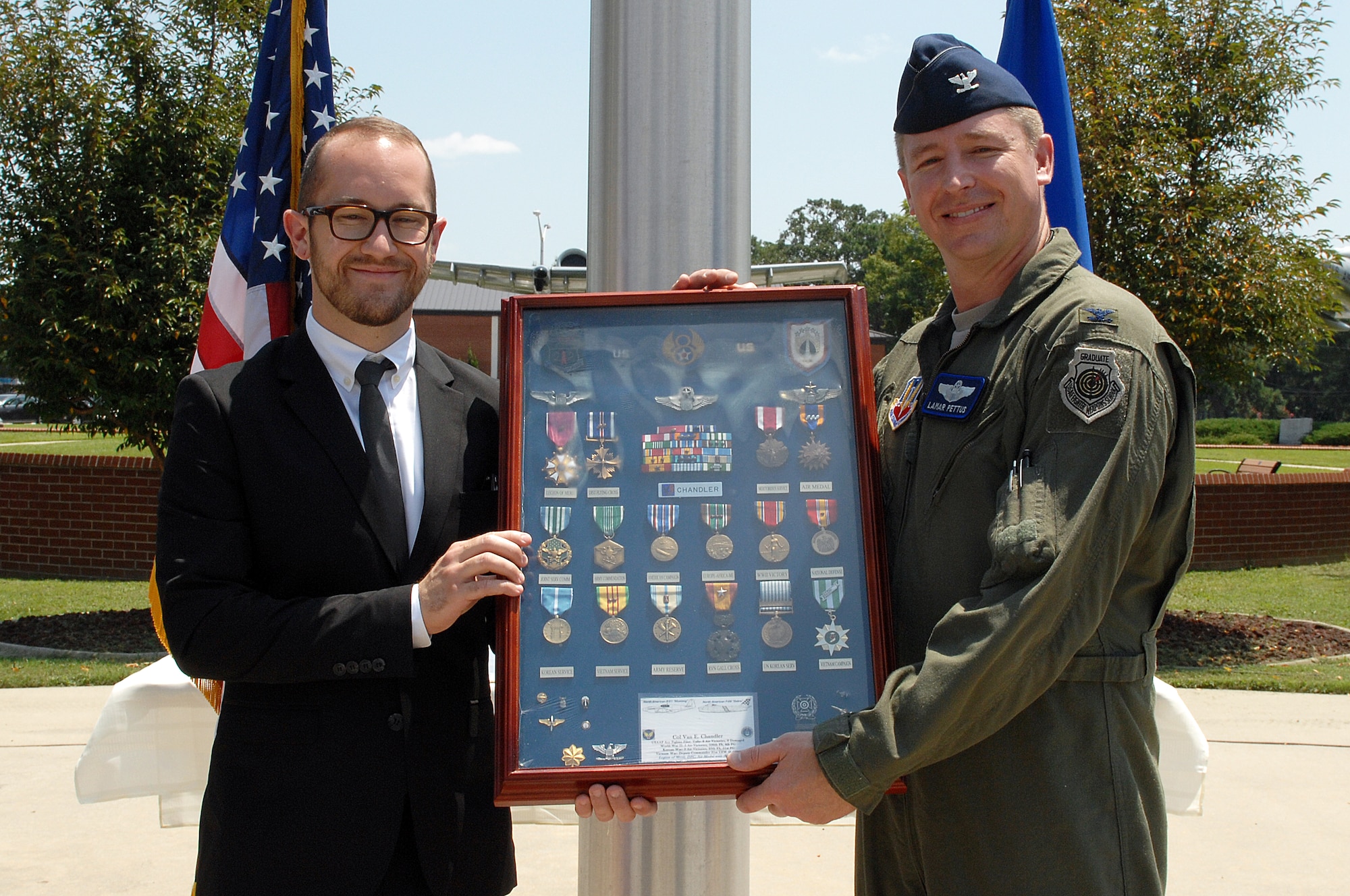Thomas Nash, grandson of retired Col. Van Chandler, presents Col. Lamar Pettus, 4th Fighter Wing vice commander, with a shadow box of his grandfather’s medals during a ceremony at Seymour Johnson Air Force Base, N.C., Aug. 5, 2013.  Among Chandler’s honors are the Legion of Merit medal with one oak leaf cluster and the Distinguished Flying Cross with two oak leaf clusters.  (U.S. Air Force photo by Airman 1st Class Brittain Crolley/Released)