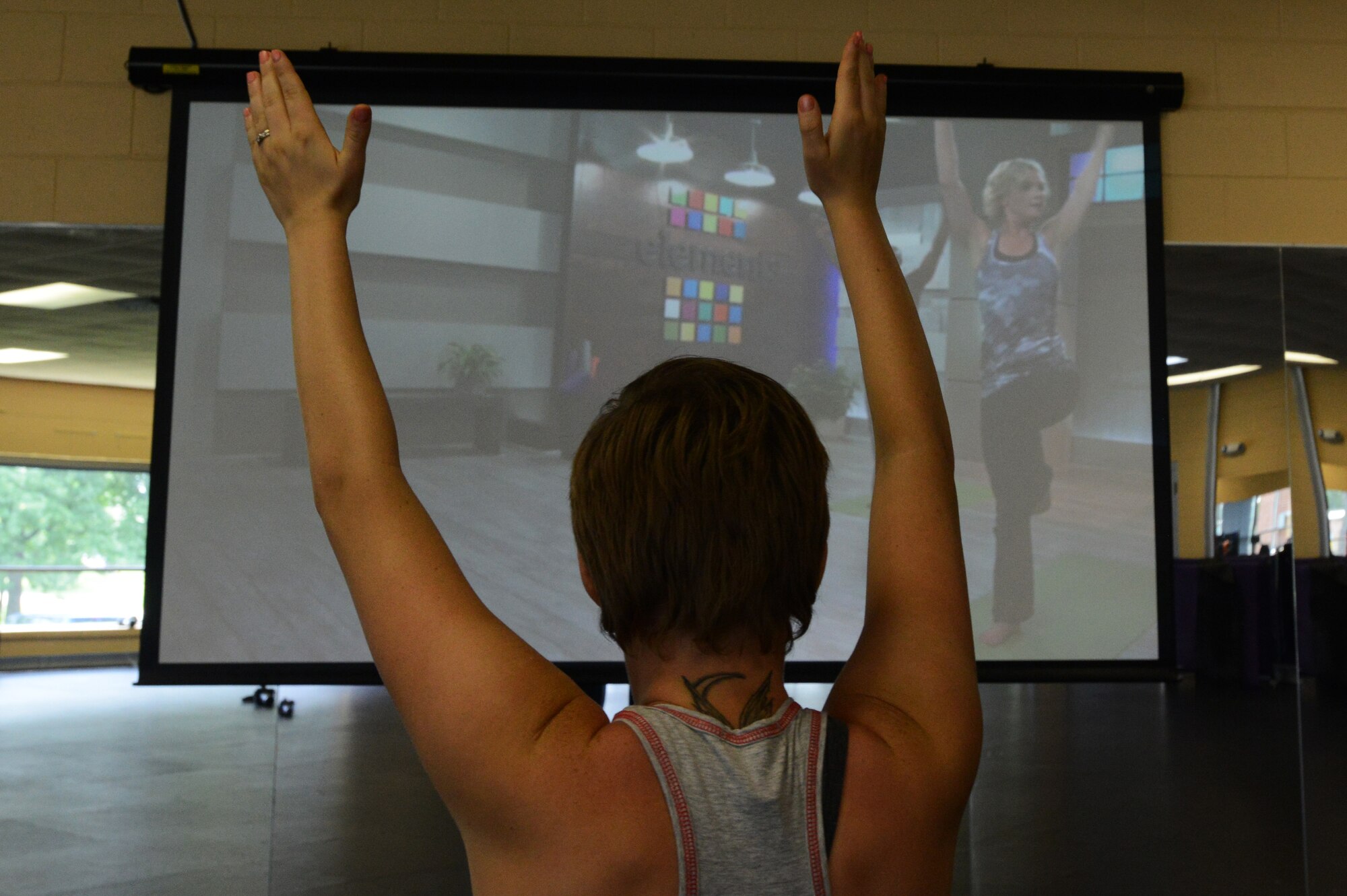 Addison Johnson, wife of Airman 1st Class Jensen Stidham, watches a “Fitness on Request” video while practicing yoga at the fitness center, Shaw Air Force Base S.C., Aug. 1, 2013.  Johnson raises her arms while following “Fitness on Request” instructors during a yoga exercise.  (U.S. Air Force photo by Airman 1st Class Jensen Stidham/ Released) 
