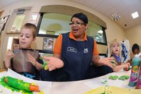 Sonia Premdas (right), a child care program assistant, at Joint Base-San Antonio-Randolph Child Development Center assists Eli Scannon July 17 with an art project. Sonia's efforts support military families living and working on base.  ( U.S. Air Force photo by Don Lindsey )