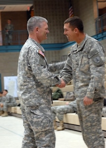 Maj. Gen. David Sprynczynatyk, North Dakota National Guard adjutant general, presents Staff Sgt. Justin J. Lampert with a commander's coin for excellence at the Fargo Armed Forces Reserve Center on April 3. Lampert led a quick reaction force team that responded to the breach at Oak Grove Lutheran School and taught helicopter sling-loading operations to fellow Guardsmen to ensure proper hook-up of 1-ton sandbags. He volunteered to fight the flood and paid his own way back to North Dakota from Fort Benning, Ga., where he was instructing Air Assault School.