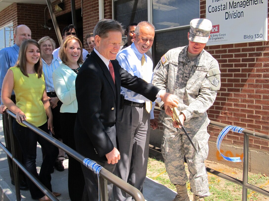 FORT HAMILTON, NY - Staff members from the Hurricane Sandy Coastal Management Division joined Vincent Grewatz, regional business director, Joe Forcina, chief of Hurricane Sandy CMD, and Brig. Gen. Kent Savre, commanding general of the North Atlantic Division of the U.S. Army Corps of Engineers July 30 to cut a ribbon signifying the opening of the Hurricane Sandy CMD's headquarters in Building 130 here. With the passage of the Hurricane Sandy Disaster Relief Appropriations Act of 2013, the U.S. Army Corps of Engineers was given the authority and funding to repair and complete ongoing coastal storm damage risk reduction projects and studies in the Northeast. The staff of approximately 20 will operate in the headquarters for the next three to five years. The team will focus on restoration of beaches and navigation channels to their pre-storm condition and to conduct studies to analyze how to promote the resiliency of the North Atlantic coast in preparation for future extreme weather.