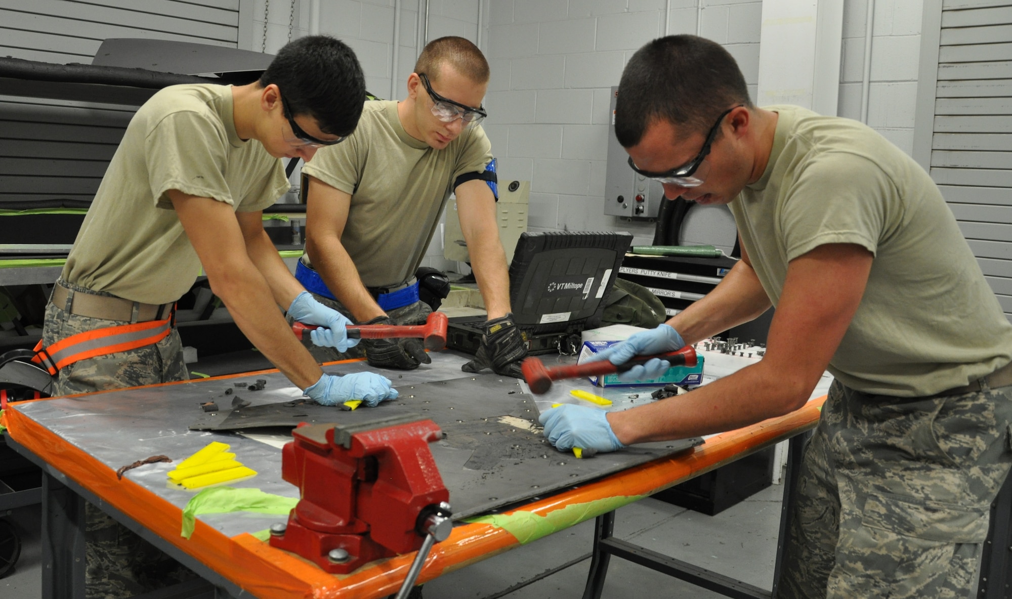 Senior Airman Zachary Kugler, 325th Maintenance Squadron Low Observable Journeyman, Airman 1st Class Keenan McCormack, 325th MXS Low Observable apprentice, and Airman 1st Class Samuel Schroeder 325th MXS Low Observable apprentice, chisel damaged coating off of a panel Aug. 1 in the LO shop at Tyndall Air Force Base. The 325th Maintenance Squadron Low Observable makes sure the F-22 Raptors at Tyndall maintain their stealth capabilities by restoring and maintaining the Low Observable coatings on the aircraft. (U.S. Air Force photo by Airman 1st Class Alex Echols)