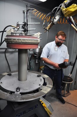 Andy Schroeder, a process engineer with the 76th PMXG, programs a robot for a plasma spray job on an F119 engine ring. Engineers write a spray program, perform a test run on a small section, send that section to the lab for testing, and then proceed with the program when they get the thumbs up. (Air Force photo by Micah Garbarino)