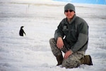 Master Sgt. Tyler Sutton, 176th Wing, Alaska Air National Guard, smiles while a penguin walks by the flight line near McMurdo Air Station, Antarctica. Sutton augmented the New York Air National Guard as an aircrew flight equipment specialist during a 30-day rotation in Antarctica supporting the National Science Foundation.