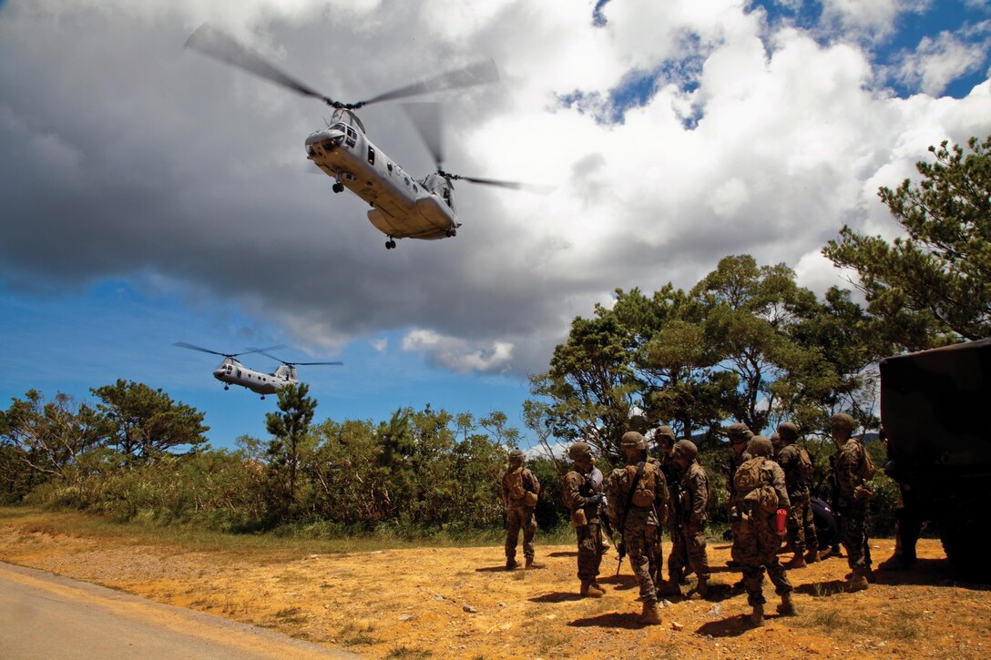 Marines watch as CH-46E Sea Knight helicopters fly over following insertion-and-extraction training July 30 at Landing Zone Falcon at the Central Training Area. The Marines were tasked with gathering enemy intelligence before calling for emergency evacuation from the area. 