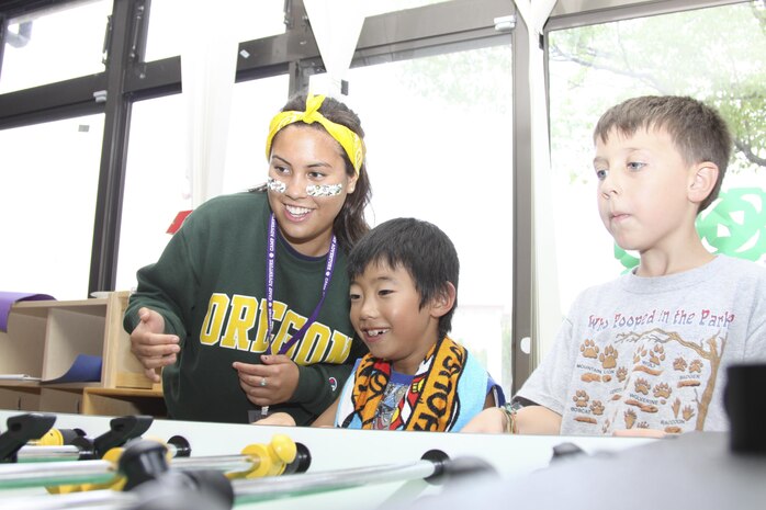 Courteney Harbour, left, a Camp Adventure staff member, teaches a Japanese child how to play foosball at the station's School Age Care Center during the Minamigouchi and Kitagouchi Iwakuni city branches visit July 30, 2013. The Minamigouchi district is for children of southern Iwakuni, and the Kitagouchi is for children from northern Iwakuni.