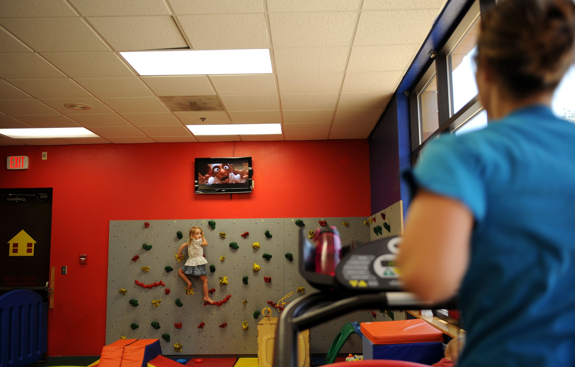 Madison Walker, daughter of Staff Sgt. Logan Walker, 42nd Electronic Combat Squadron, utilizes the kid-friendly rock climbing wall as her mother, Sarah Walker, runs on the treadmill in the Munchkin Room at the Benko Fitness and Sports Center at Davis-Monthan Air Force Base, Ariz., Aug. 7, 2013. The Munchkin Room, the only child-friendly area at the gym, allowed Sarah to bring her daughter and her son, Liam, to the gym with her while her husband is deployed. (U.S. Air Force photo by Airman 1st Class Saphfire Cook/Released)